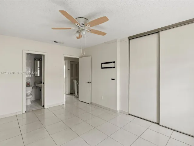 Room featuring large-format tile flooring, a multi-blade ceiling fan with integrated light fixture, and dual sliding closet doors