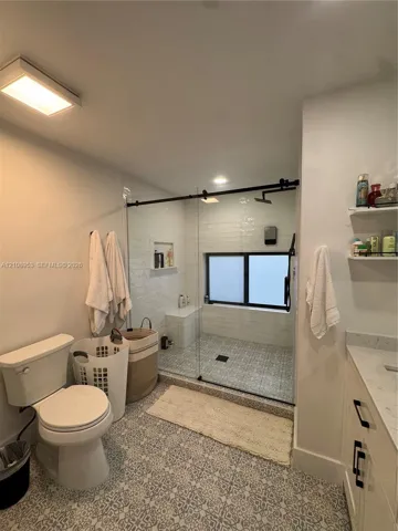 Bathroom featuring a walk-in shower with glass enclosure, built-in bench, patterned tile flooring, and stone-top vanity with black hardware