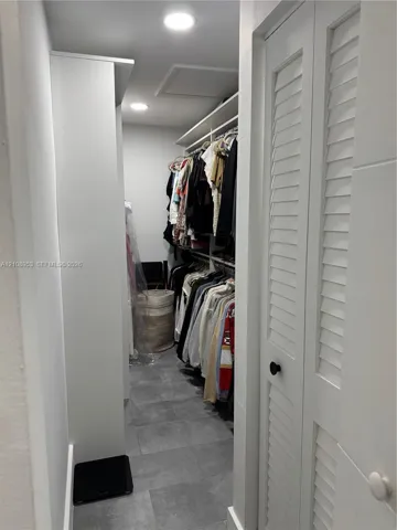 Walk-in storage space featuring ceramic tile flooring, built-in shelving, recessed lighting, and white louvered doors