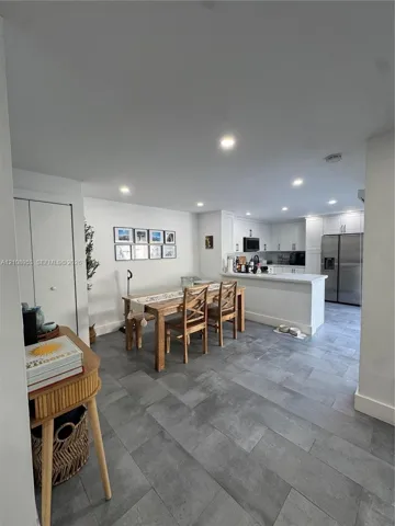 Kitchen featuring white shaker-style cabinetry, stainless steel appliances, and a breakfast bar peninsula, complemented by grey tile flooring and recessed lighting