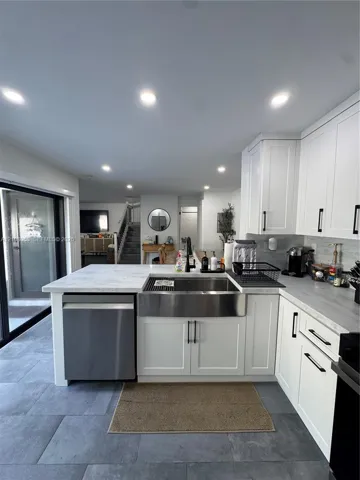 Kitchen featuring white shaker-style cabinetry, stainless steel apron-front sink, stone-finish countertops, recessed lighting, and large-format tile flooring