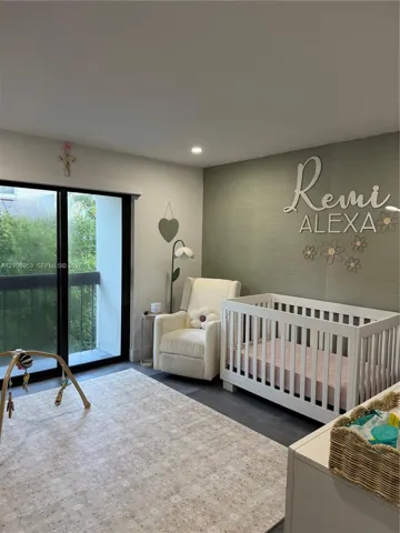 Room featuring a textured olive-toned accent wall, sliding glass door with black framing, and dark wood-finish flooring