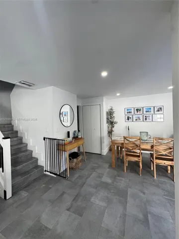 Large-format neutral-tone tile flooring, recessed ceiling lighting, and staircase with dark stone-finish treads and white wooden railings