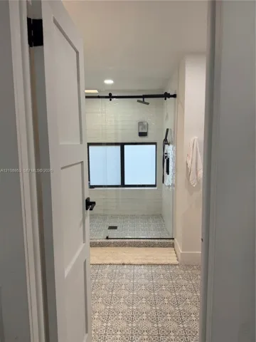 Walk-in shower with patterned tile flooring, white horizontal subway tile wall surround, black sliding glass door hardware, and black plumbing fixtures