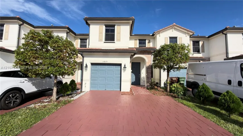 Two-story townhouse exterior featuring light-toned stucco siding, a paved driveway, and an integrated single-car garage with a paneled door