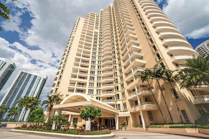 High-rise exterior featuring curved balconies, a covered entrance porte-cochère, and manicured landscaping