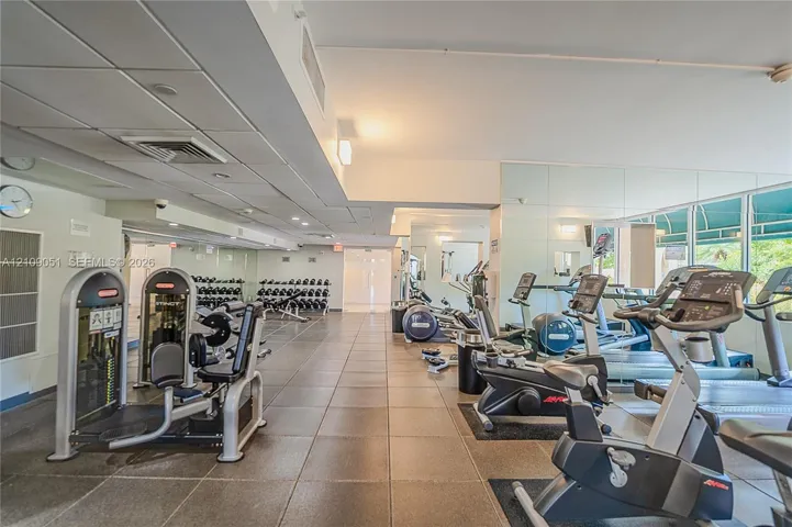 Fitness center featuring large-format tile flooring, mirrored walls, recessed lighting, and expansive windows