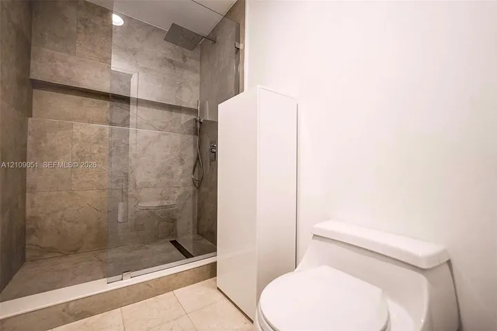 Walk-in shower featuring oversized stone-finish wall tiles, a built-in recessed shelf, a frameless glass enclosure, and a ceiling-mounted rainfall showerhead