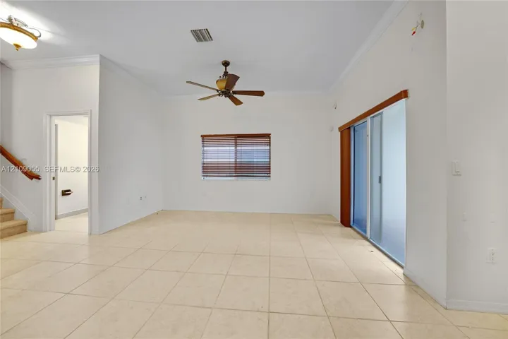 High-ceilinged interior featuring tile flooring, crown molding, a central ceiling fan, and sliding glass doors with wood-toned trim
