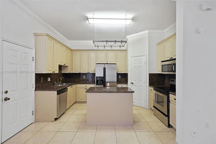 Kitchen featuring light-toned cabinetry, a center island with a stone-finish countertop, stainless steel appliances, and a ceiling-mounted hanging rack