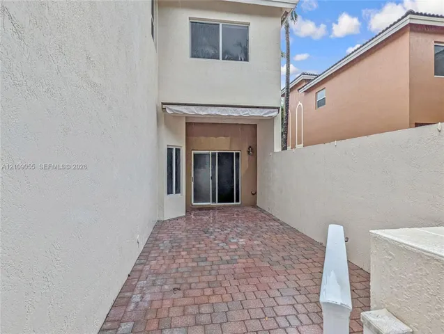 Private rear patio featuring paver hardscaping, retractable awning, sliding glass door, and stucco wall enclosure