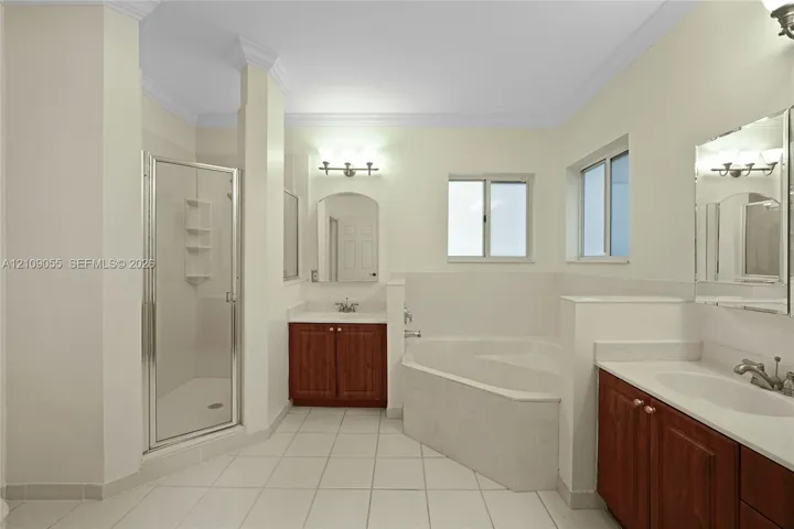 Bathroom featuring dual wooden cabinetry with light-toned countertops, a glass-enclosed shower, a corner soaking tub, and tile flooring