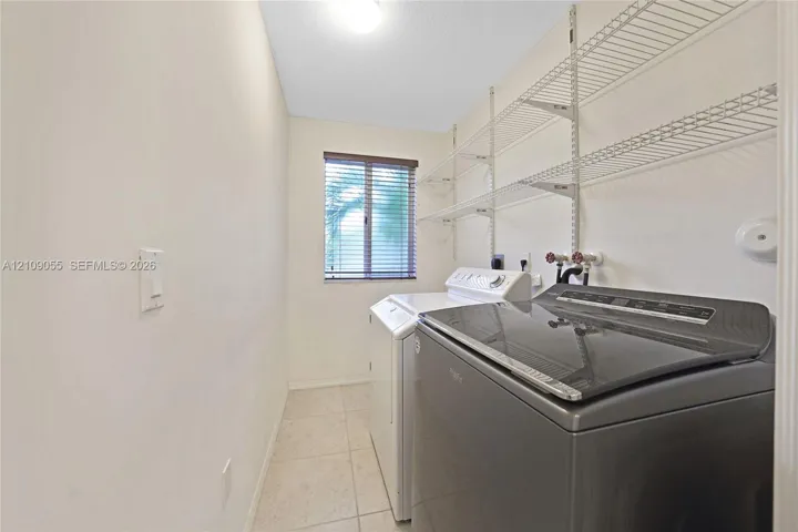 Utility room featuring ceramic tile flooring, a window with horizontal blinds, and metal wall-mounted shelving