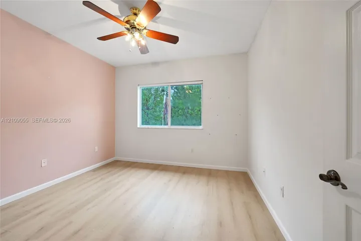 Room featuring wood-finish flooring, a ceiling fan with integrated lighting, and a window with a natural exterior backdrop