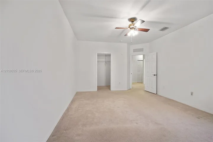 Neutral-toned wall-to-wall carpeting, ceiling fan with integrated lighting, and walk-in closet with built-in shelving
