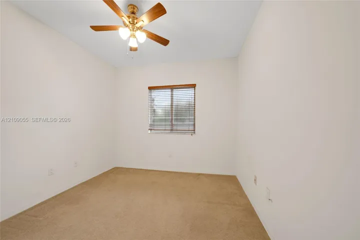 Neutral-toned carpeted flooring, window with installed horizontal blinds, and a central ceiling fan with integrated lighting