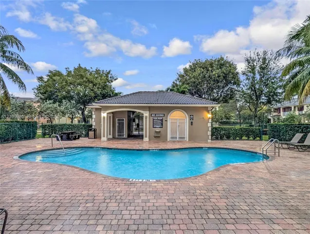 Free-form swimming pool featuring a brick-paver deck, built-in steps, metal railings, and a covered pavilion with arched entryways