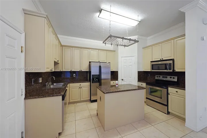 Kitchen featuring cream-colored cabinetry, stone countertops, stainless steel appliances, a central island, and an overhead hanging rack