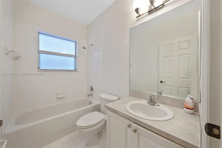 Bathroom featuring a single-sink vanity with light-toned solid surface countertop, tub-shower combination with tile surround, large wall-mounted mirror, and overhead vanity lighting
