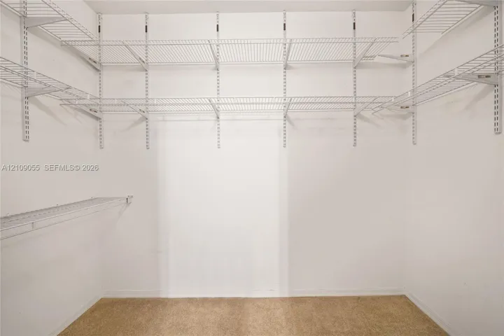 Storage area featuring white wall-mounted wire shelving systems and neutral-tone carpeting