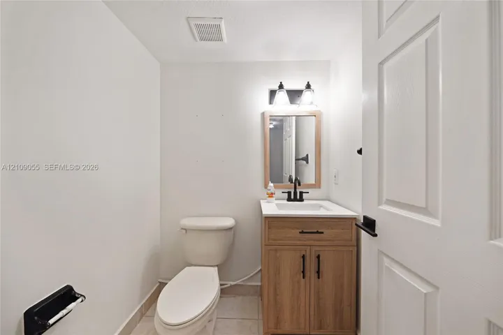 Wood-finish vanity cabinet with a stone-top integrated sink, matte black hardware, dual-light fixture, and framed wall mirror