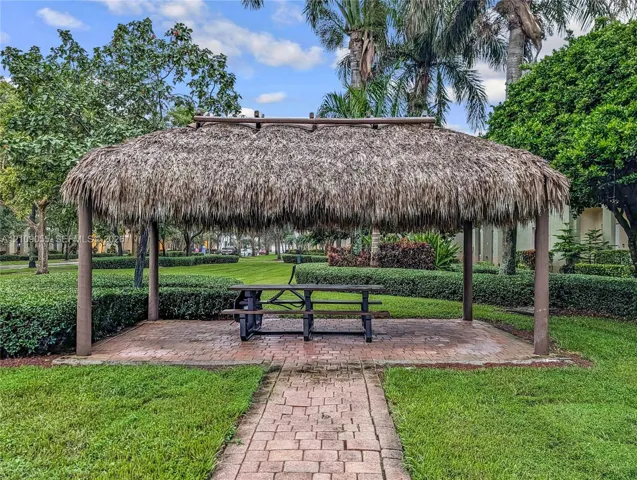 Thatched-roof tiki hut featuring a brick-paved patio, brick walkway, and mature perimeter landscaping