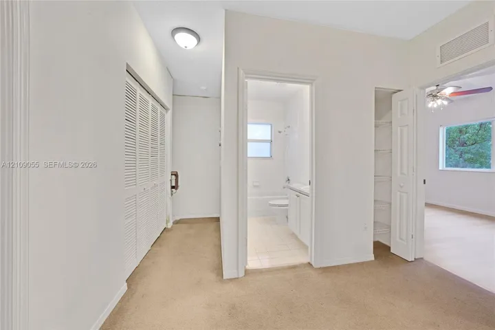 Neutral carpeting, louvered bi-fold closet doors, built-in shelving, and tile flooring within the restroom