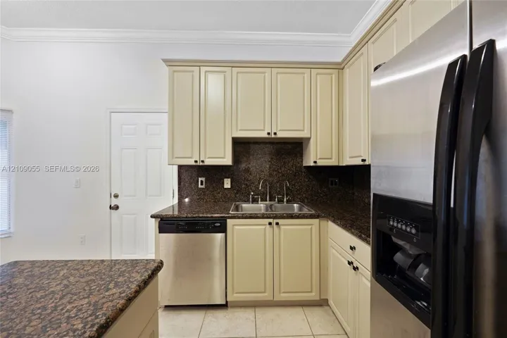 Kitchen featuring shaker-style cabinetry, stone countertops, double-basin undermount sink, stainless steel dishwasher, and stainless steel refrigerator