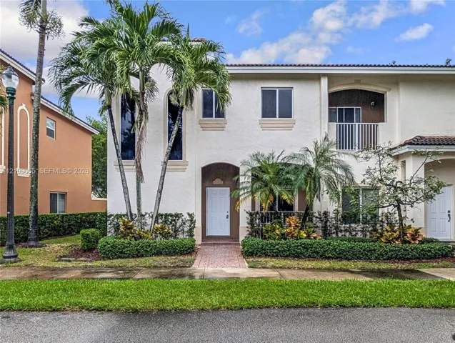 Two-story stucco exterior featuring arched windows, a private second-story balcony with metal railings, and a paver walkway leading to the front entry