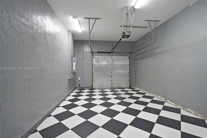 Enclosed garage featuring a checkerboard-patterned floor, painted concrete walls, and dual overhead light fixtures