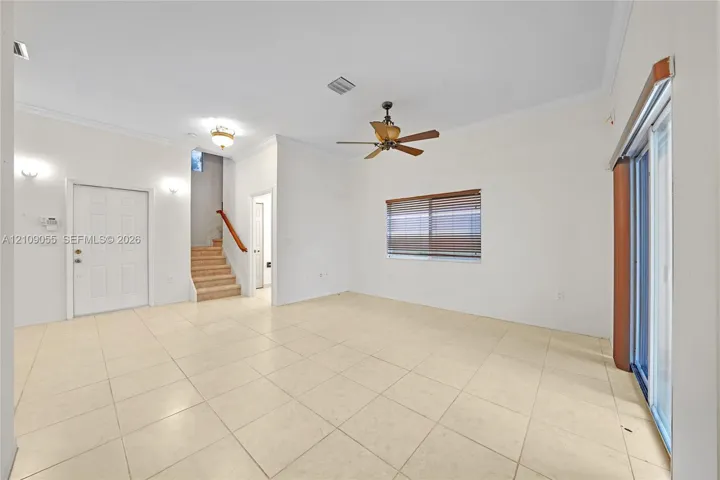 Neutral tile flooring, ceiling fan with light fixture, sliding glass doors, carpeted staircase with wood handrail, and recessed wall sconces