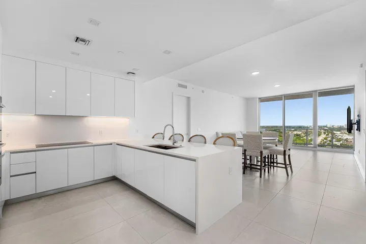 Modern kitchen featuring flat-panel white cabinetry, quartz countertops, a central island with an integrated sink, recessed lighting, and expansive floor-to-ceiling windows