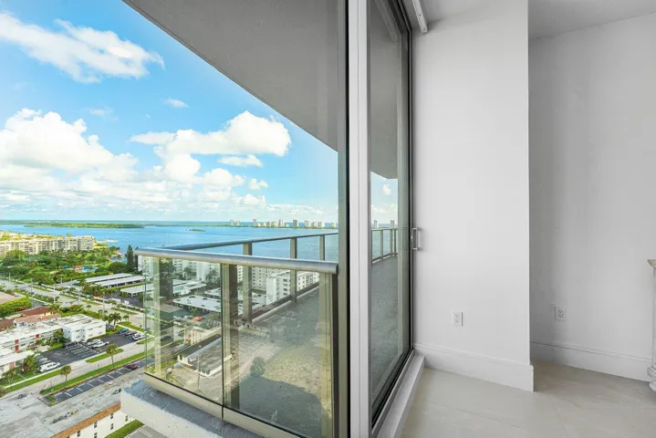 Full-height sliding glass doors opening to a glass-paneled balcony overlooking the water