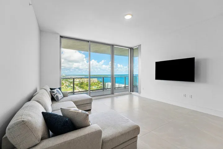 Floor-to-ceiling sliding glass doors, ceramic tile flooring, and a glass-paneled balcony featuring coastal and urban scenery