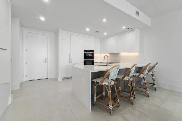 Contemporary kitchen featuring high-gloss cabinetry, stone-surface countertops, a waterfall-edge island with seating, built-in stainless steel appliances, and large-format tile flooring