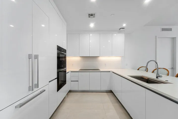 Kitchen featuring high-gloss cabinetry, stone countertops, integrated wall ovens, a cooktop, and an undermount sink with a gooseneck faucet