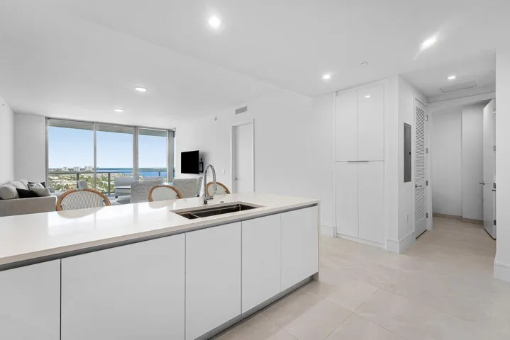 Kitchen featuring a waterfall-edge stone island, undermount stainless steel sink, floor-to-ceiling cabinetry, recessed lighting, and large-format tile flooring