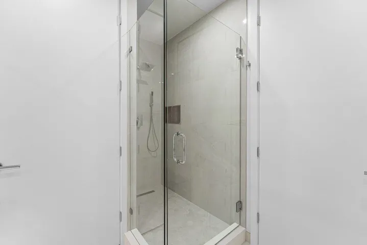 Walk-in shower featuring a glass enclosure with polished hardware, oversized wall tile, rainfall showerhead, and wall-mounted hand shower