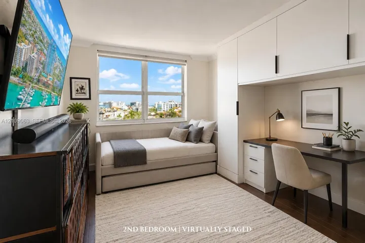 Room featuring wood-finish flooring, extensive built-in white cabinetry, integrated desk workspace with drawer storage, and a large window