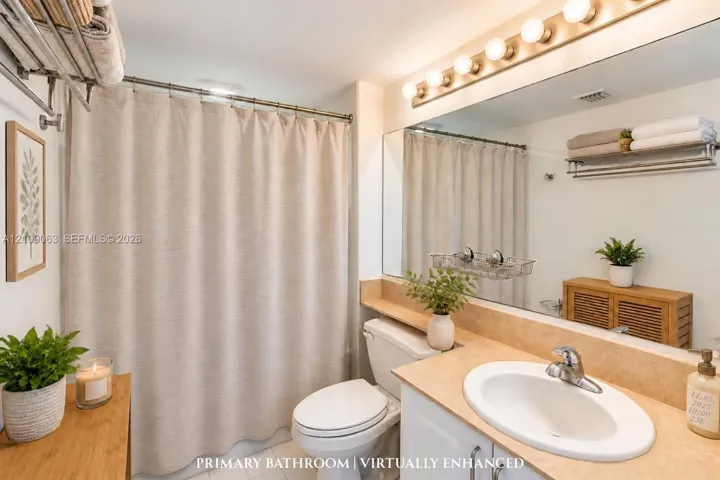 Bathroom featuring a vanity with a neutral-tone countertop, oval undermount sink, expansive wall-to-wall mirror, multi-bulb vanity lighting, and a shower-tub combination with a wall-mounted storage rack