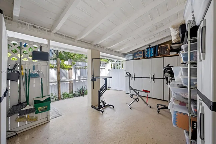 Covered patio area featuring a white-painted exposed beam ceiling, concrete flooring, lattice wall paneling, and a secured gate