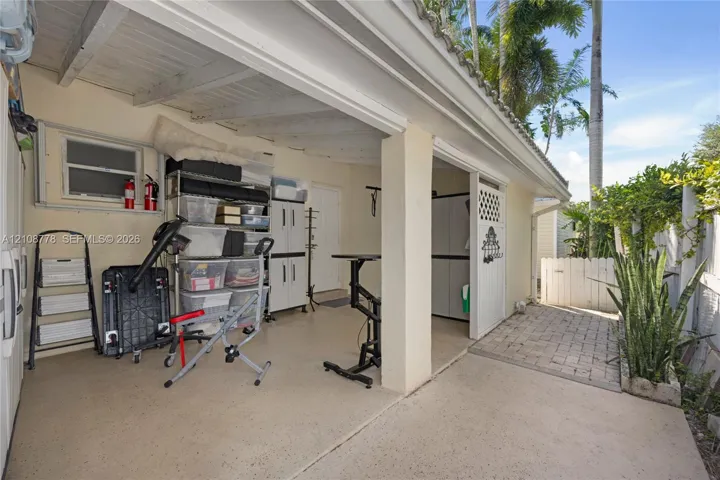 Covered carport featuring an epoxy-coated concrete floor, exposed beam ceiling, and stone paver entryway