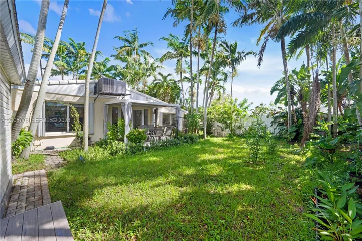 Expansive backyard featuring a lush lawn, mature palm trees, a covered patio, and brick paver pathways