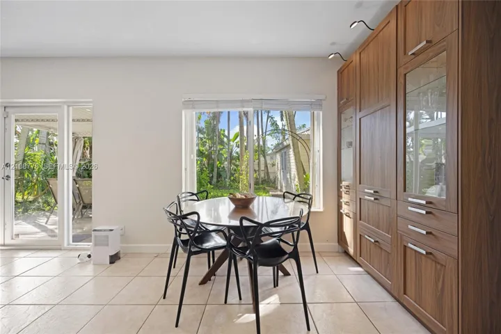 Full-wall wood cabinetry featuring integrated storage, glass-front display sections, and overhead directional lighting, complemented by tile flooring, a large picture window, and a glass-panel exterior door