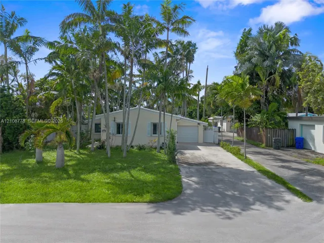 Exterior facade featuring a concrete driveway, an attached garage, mature palm trees, and established landscaping