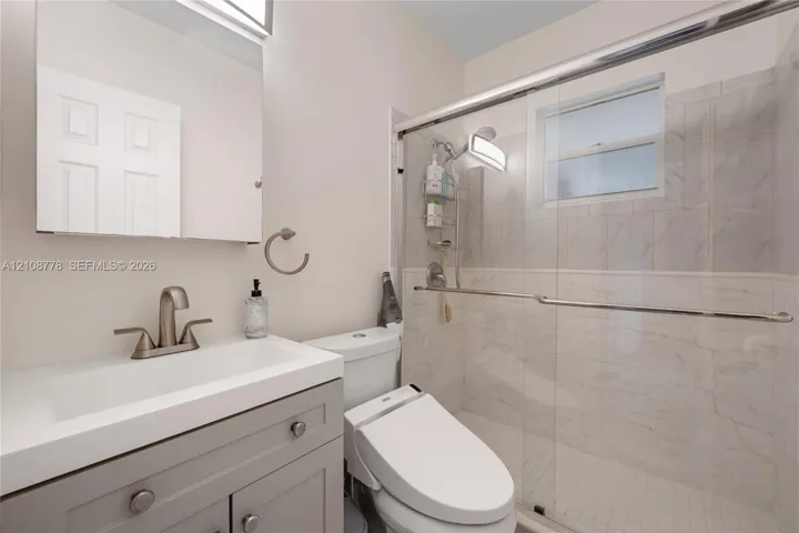 Bathroom featuring a gray vanity with a white rectangular sink, a glass-enclosed shower with tiled surround, and a wall-mounted medicine cabinet