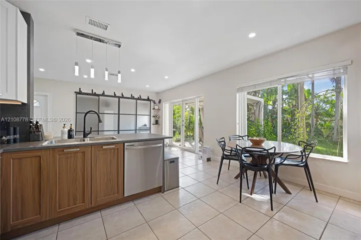 Kitchen featuring a wood-finish cabinetry island, matte black faucet, stainless steel dishwasher, glass-paned sliding door partition, and recessed ceiling lighting