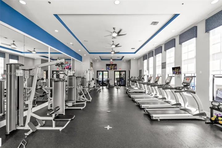 Fitness center featuring rubber flooring, recessed ceiling lighting, multiple ceiling fans, wall-to-wall mirrors, and a row of cardio equipment