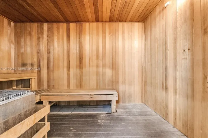 Sauna featuring wood-plank walls and ceiling, tiered wooden bench seating, and an integrated stone heating unit