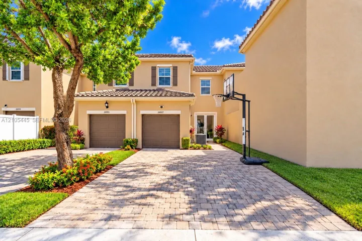 Two-story stucco exterior featuring a tiled roof, dual-bay garage, paver driveway, and manicured landscaping